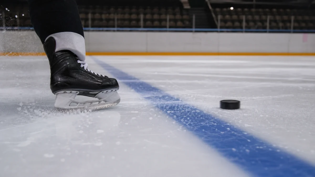 Skridsko och puck på var sin sida av hockeyrinkens blålinje